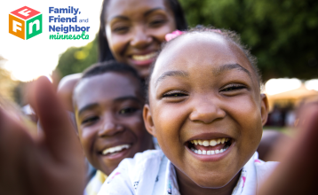 Kids smiling in the camera with adult smiling behind them