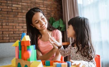 Daycare setting with early childhood educator and child playing with blocks
