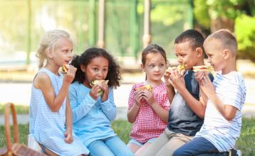Four kids between the ages 5-8 having sandwiches in a park on a sunny day. 