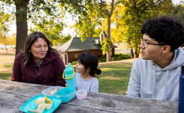 A mom and her daughter and son sitting at a picnic table. 