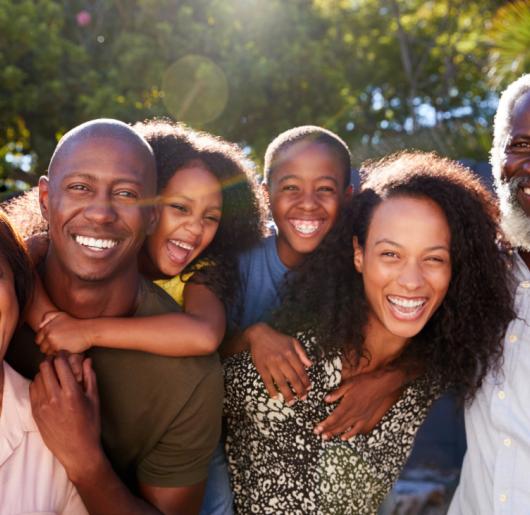 Outdoor portrait of multi-generation family in garden at home against flaring sun.