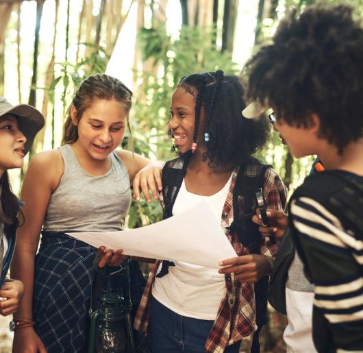 A group of teenagers looking at a map while exploring nature together at summer camp.