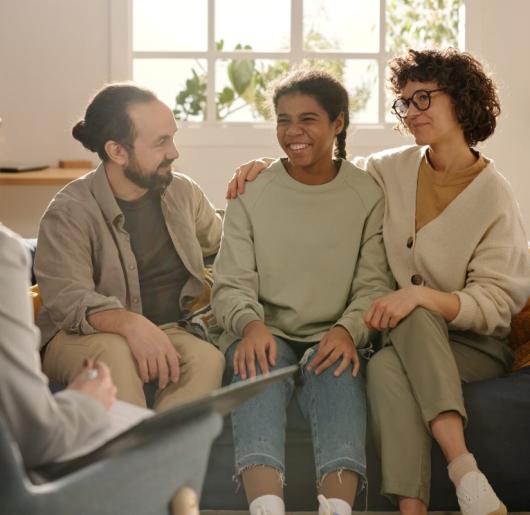 Adults sitting on sofa with a teen girl and talking to social worker during meeting