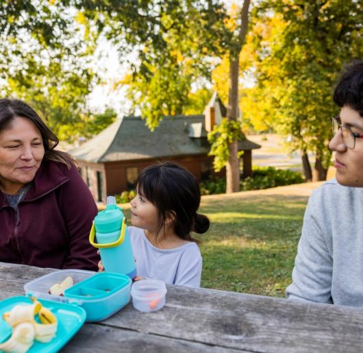 A mom and her daughter and son sitting at a picnic table. 