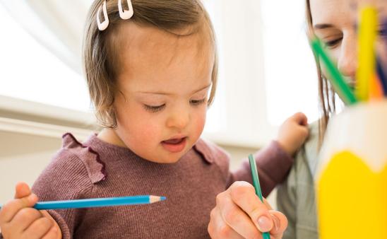 Adult shows a child how to use a colored pencil