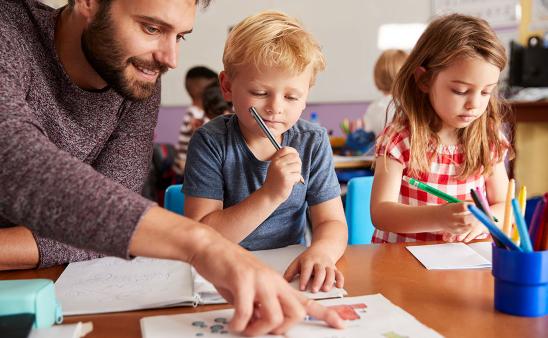 A male teacher points to a paper while helping a young student