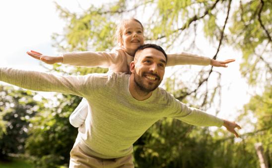 Child on dad's back, both pretending to be airplanes
