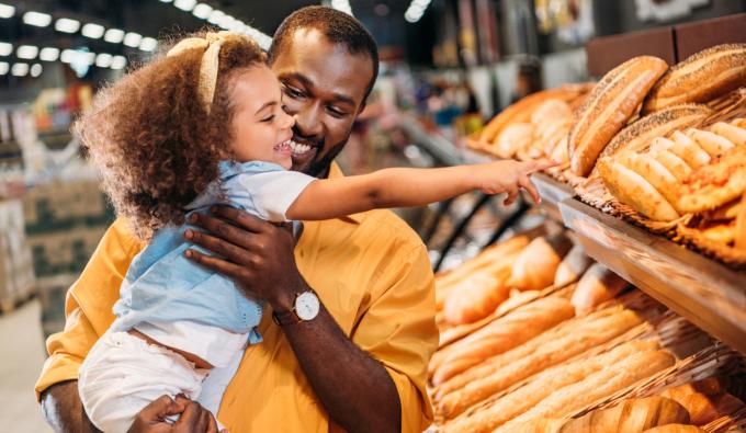 A young child pointing by finger at pastry to father in supermarket.