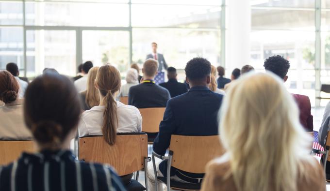 A man giving a speech in front of a crowd in a room.