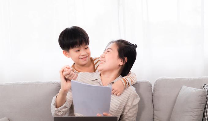 A mom sitting on sofa with her son while she is typing on laptop.