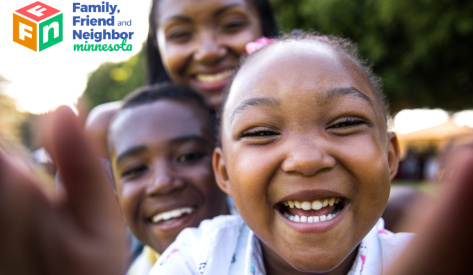 Kids smiling in the camera with adult smiling behind them