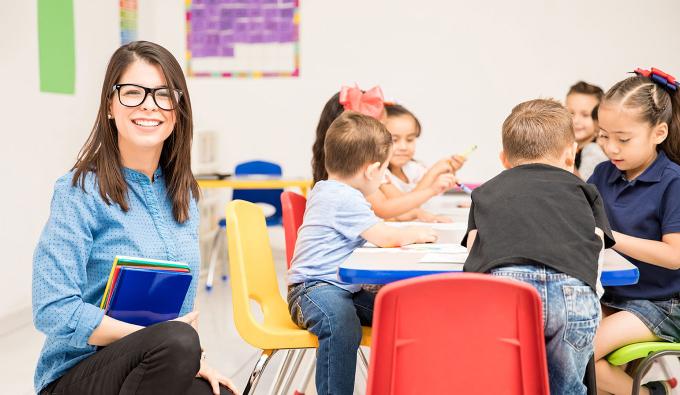 An educator kneels next to a table with young children