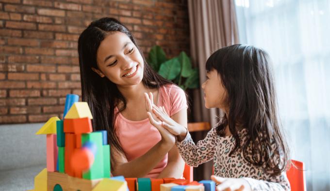 Daycare setting with early childhood educator and child playing with blocks