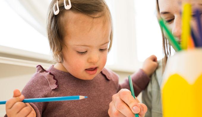 Adult shows a child how to use a colored pencil