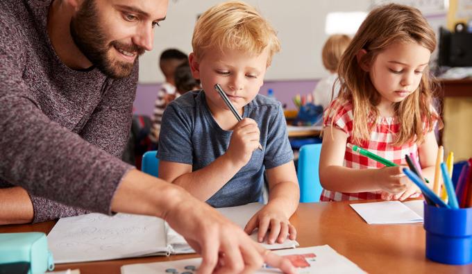 A male teacher points to a paper while helping a young student