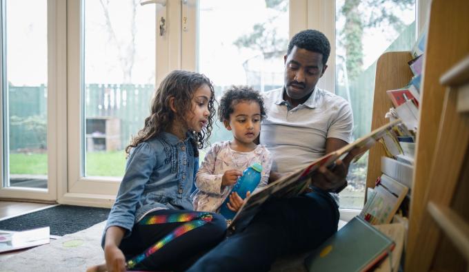 Two young girls read with their dad