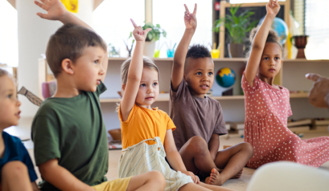 Children seated on the floor with their hands raised.