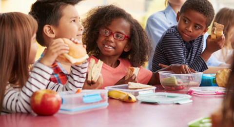 A row of children eating lunch at a school lunch table. 