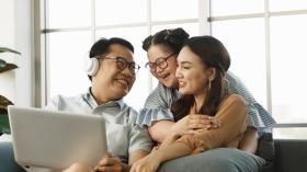 Happy family of three sitting together on couch with laptop.