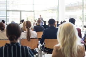 A man giving a speech in front of a crowd in a room.