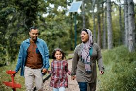 Mom, dad, and girl walk on a trail. Dad is holding a toy airplane.