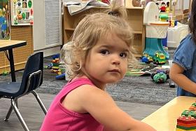 Toddler in a pink shirt next to a shape stacking toy