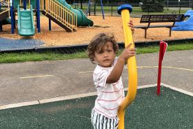 Boy holds onto a yellow pole at the playground