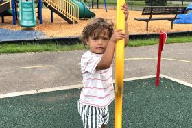 Boy holds onto a yellow pole at the playground