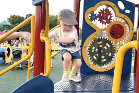 Toddler in hat climbs onto playground, passing by gear toys