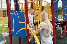 Girl goes down the playground stairs while her mom stands close by, ready to help