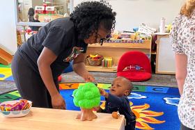 Baby reaches for a tree toy while his mom helps