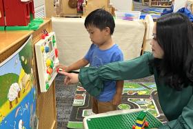 Mom and toddler play with a toy hanging on the wall
