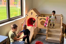 Toddlers playing on an indoor wooden climber with a slide