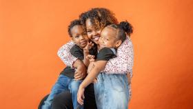 Mom hugs her son and daughter with their faces pressed against hers, smiling at the camera