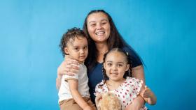 A mom smiles and poses with her arms around her two children