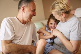 Two older caregivers laugh with a young boy on the couch